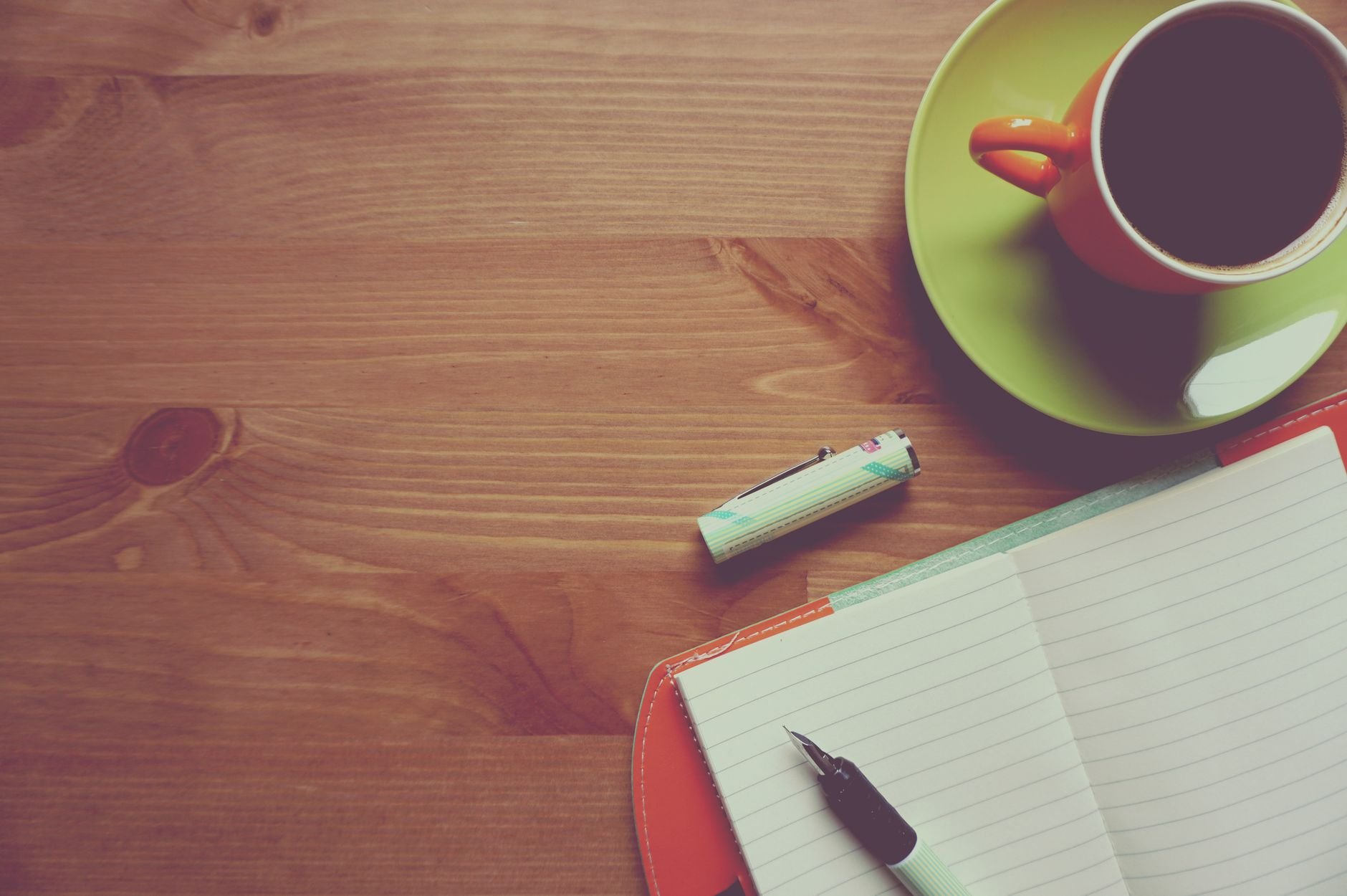 A warm workspace with a journal, pen, and coffee on a wooden surface